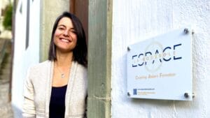 Portrait de Lisa Burri, fondatrice d’Espace La Boussole, debout devant l’entrée de son espace d’accompagnement à Fribourg. Cette image reflète l’accueil chaleureux et bienveillant réservé aux personnes en quête de clarté, de recentrage ou de mieux-être. Lisa y propose des accompagnements personnalisés en astrologie, Human Design, coaching de vie et nutrition, en présentiel à Fribourg ou en ligne. Cette photo illustre le lien humain et l’engagement dans un accompagnement sensible, concret et profondément aligné avec les besoins de chaque personne.